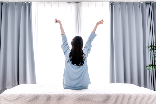 朝日の中でベッドの上で伸びをする女性